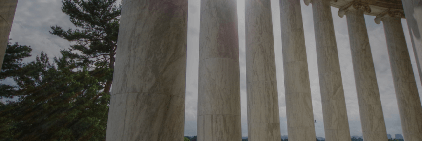 Marble columns foregrounded against trees and a cloudy sky.