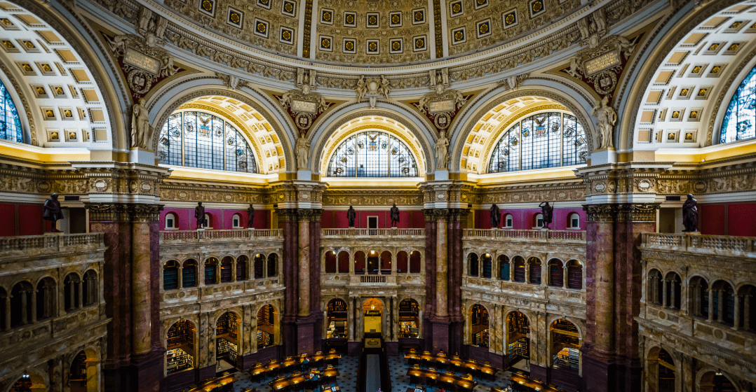 Image of the rotunda of the Library of Congress, called the Reading Room, with large columns, statues, and ornamented arched windows.