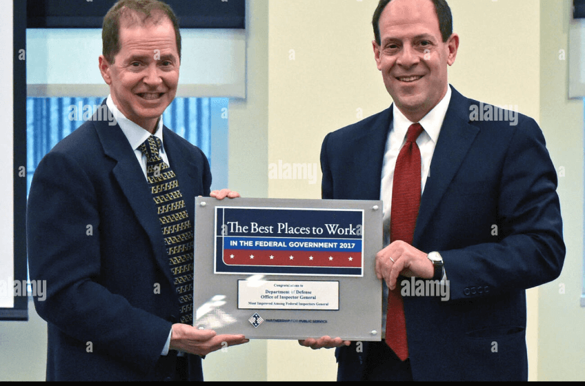 Two men in business stand holding either side of a plaque, which reads 