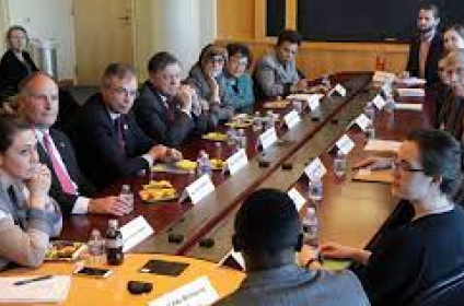 Professionals at a meeting seated around a long oval table.