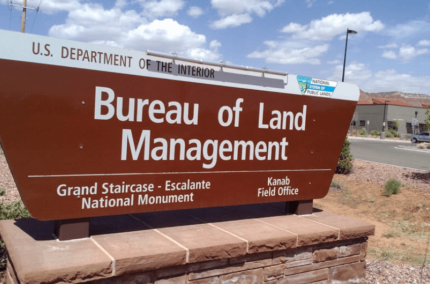 A free-standing sign by the roadside: US Department of the Interior. Bureau of Land Management. Grand Staircase-Escalante National Monument. Kanab Field Office.