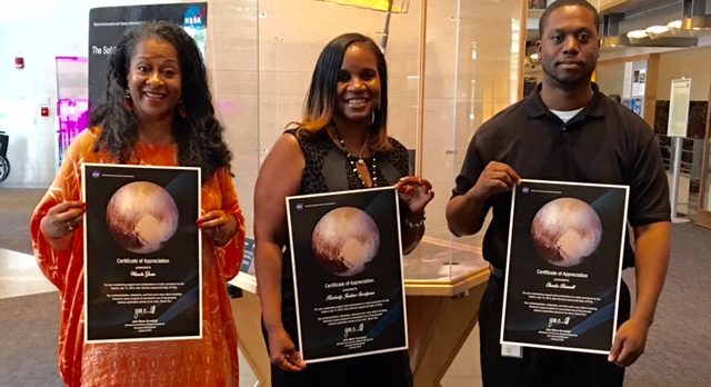 The NASA team--Wanda, Kimberly and Charles--holding posters with a photo of Pluto on them.