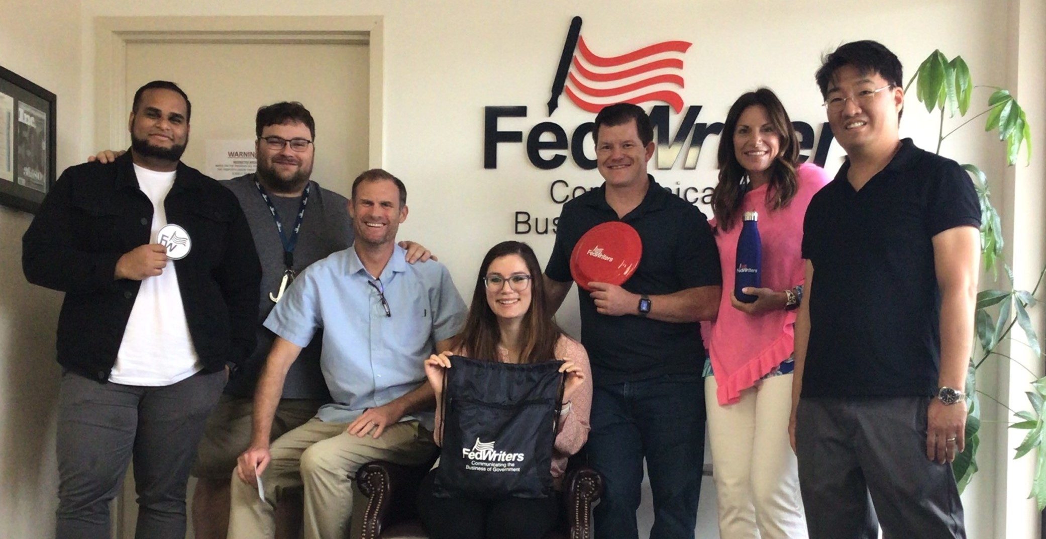 Subhaga Weerasinghe, Marc Fain, Eric Stone, Abigail Casas, Anthony Stong, Maryanne Vaughn, and Mitchell Cho posing in the FedWriters lobby holding some swag.