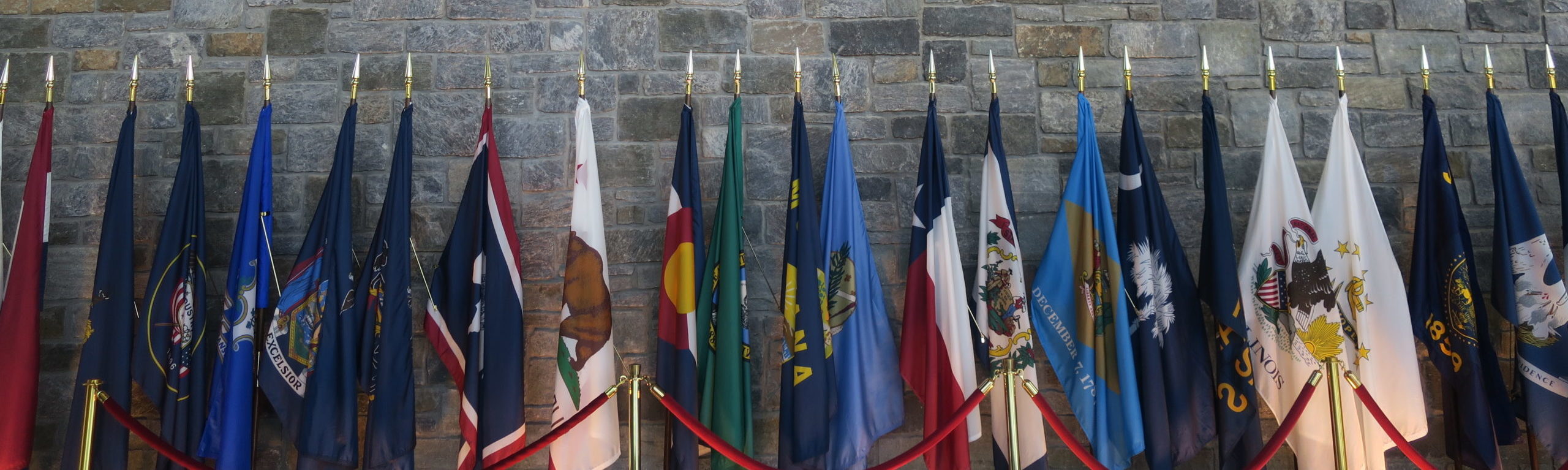 About 20 US state flags on stands lined up in a row.