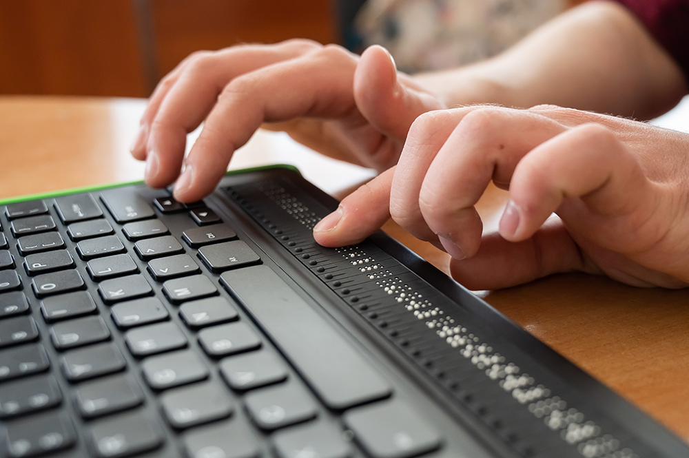 A blind man uses a computer with a Braille display and a computer keyboard. Inclusive device